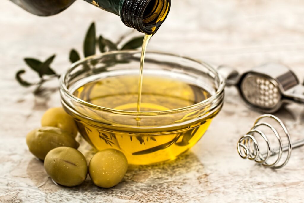 olive oil being poured into a small glass bowl with three pitted olives hugging the bowl and an olive branch subtly in the background | Busy Life Healthy Wife holistic healing practitioner