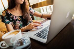 Image of a woman in a flowering top on a silver apple laptop with a latte beside her to emphasize the post - 5 reasons why customer service is still important by Busy Life Healthy Wife - spiritual business coach and holistic healer