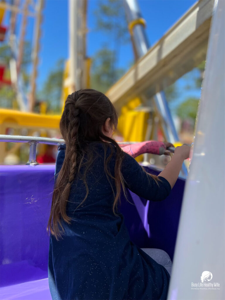a little girl with long brown hair and in a blue dreass overlooks the purple seat on a ferris wheel at the Strawberry Festival Busy Life Healthy Wife - Holistically create marketing that's effortlessly woowoo, effortlessly you